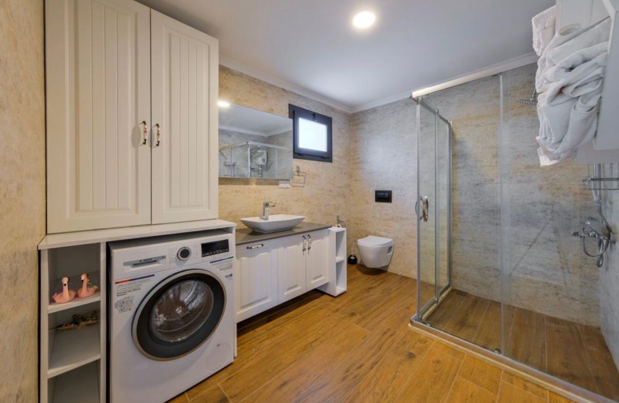 Ein modernes Badezimmer mit Waschmaschine, Waschbecken, Toilette und einer Duschkabine.
