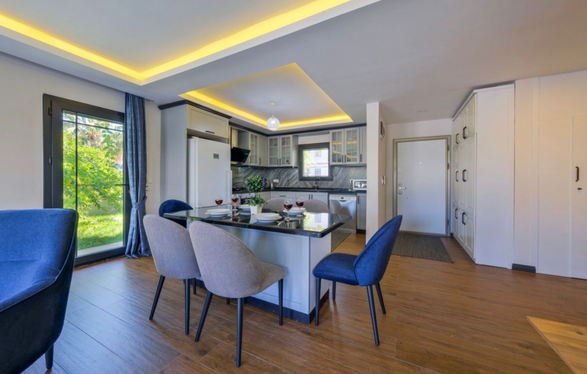 Une cuisine moderne dotée d’un îlot central, de chaises de salle à manger et offrant une vue sur la verdure à l’extérieur.