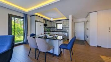Une cuisine moderne dotée d’un îlot central, de chaises de salle à manger et offrant une vue sur la verdure à l’extérieur.