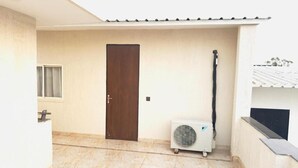 A room with a tiled floor, a door, a window with curtains, and an air conditioning unit. - Fortune Home Service Apartment Studio, J-267 Saket (New Delhi)