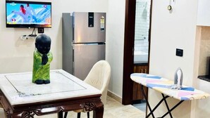 A room with a dining table, a television, a refrigerator, and an ironing board. - Fortune Home Service Apartment Studio, J-267 Saket (New Delhi)