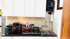 A compact kitchen with white cabinets, a gas stove, a coffee maker, and a sink. - Fortune Home Service Apartment Studio, J-267 Saket (New Delhi)