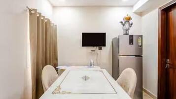 A room with a dining table, chairs, a flat-screen TV, a refrigerator, and a door.