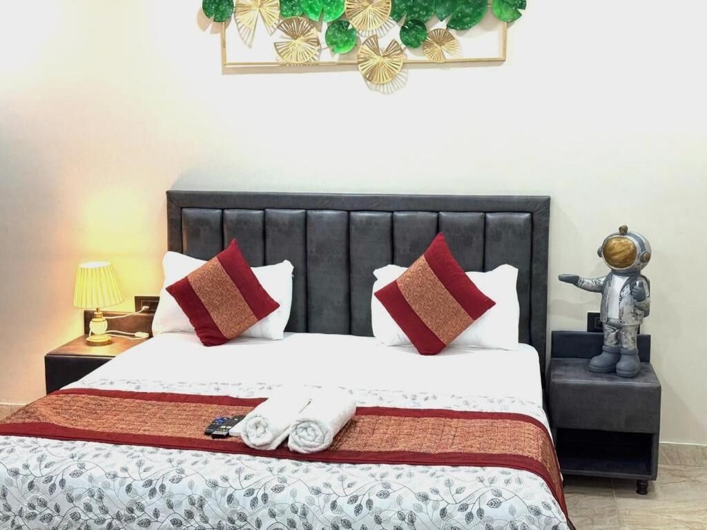 A neatly made bed with a patterned bedspread, two decorative pillows, a remote control, and a folded towel on a bedside table.