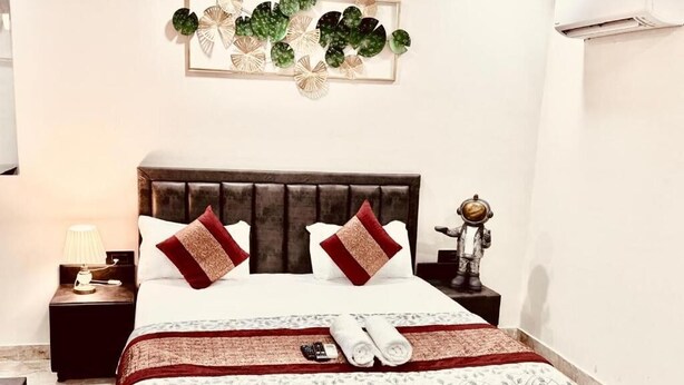 A hotel room with a bed, a nightstand, a lamp, and a decorative wall piece. - Fortune Home Service Apartment Studio, J-267 Saket (New Delhi)