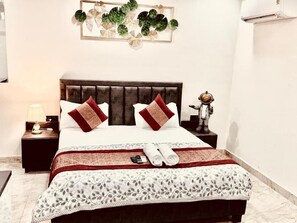 A hotel room with a bed, a nightstand, a lamp, and a decorative wall piece. - Fortune Home Service Apartment Studio, J-267 Saket (New Delhi)
