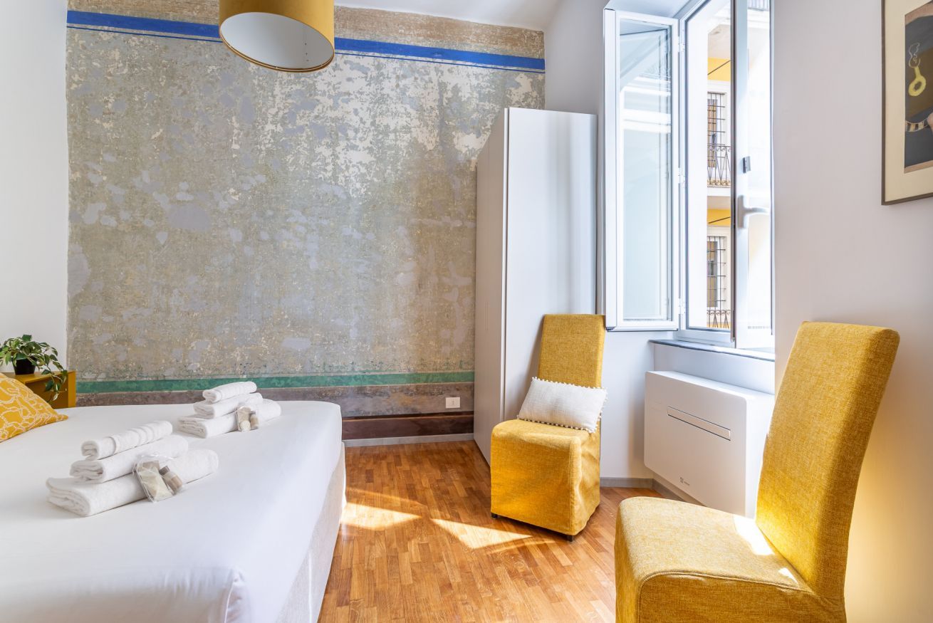 Ein Hotelzimmer mit einem Bett, zwei Stühlen, einem Fenster und einer Wand mit strukturierter Oberfläche.