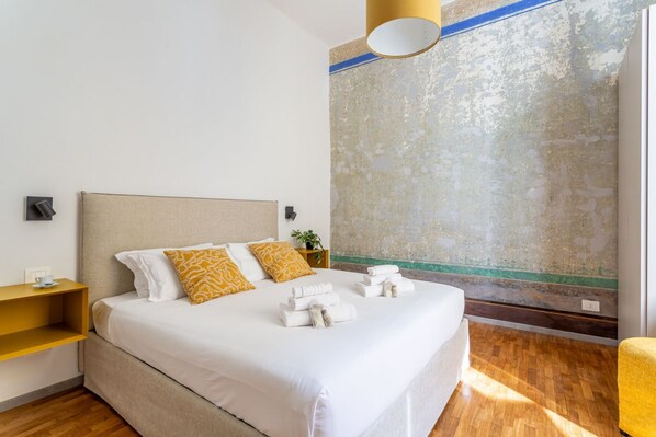 Habitación de hotel con cama, mesita de noche, lámpara de pared y vistas al exterior.