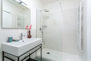 Un baño moderno con lavamanos blanco, espejo y ducha con mampara de vidrio.