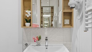 A bathroom with a white sink, a mirror, a hairdryer, and a shelf with a potted orchid and a box. - Wolska Studio Apartments by Solarento (Warsaw)