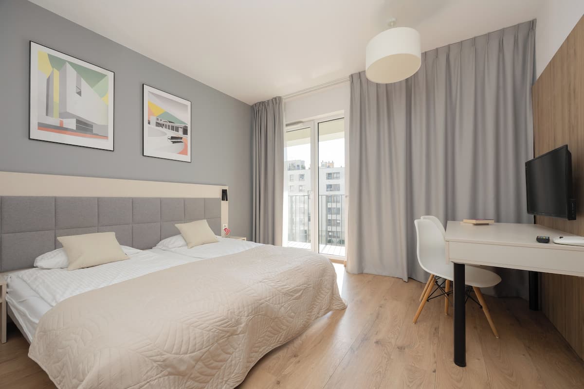 A modern hotel room with a large bed, a desk, a television, and two framed artworks on the wall.