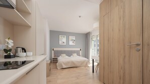 A modern hotel room with a kitchenette, a bed with a grey headboard, and a wooden wardrobe. - Wolska Studio Apartments by Solarento (Warsaw)