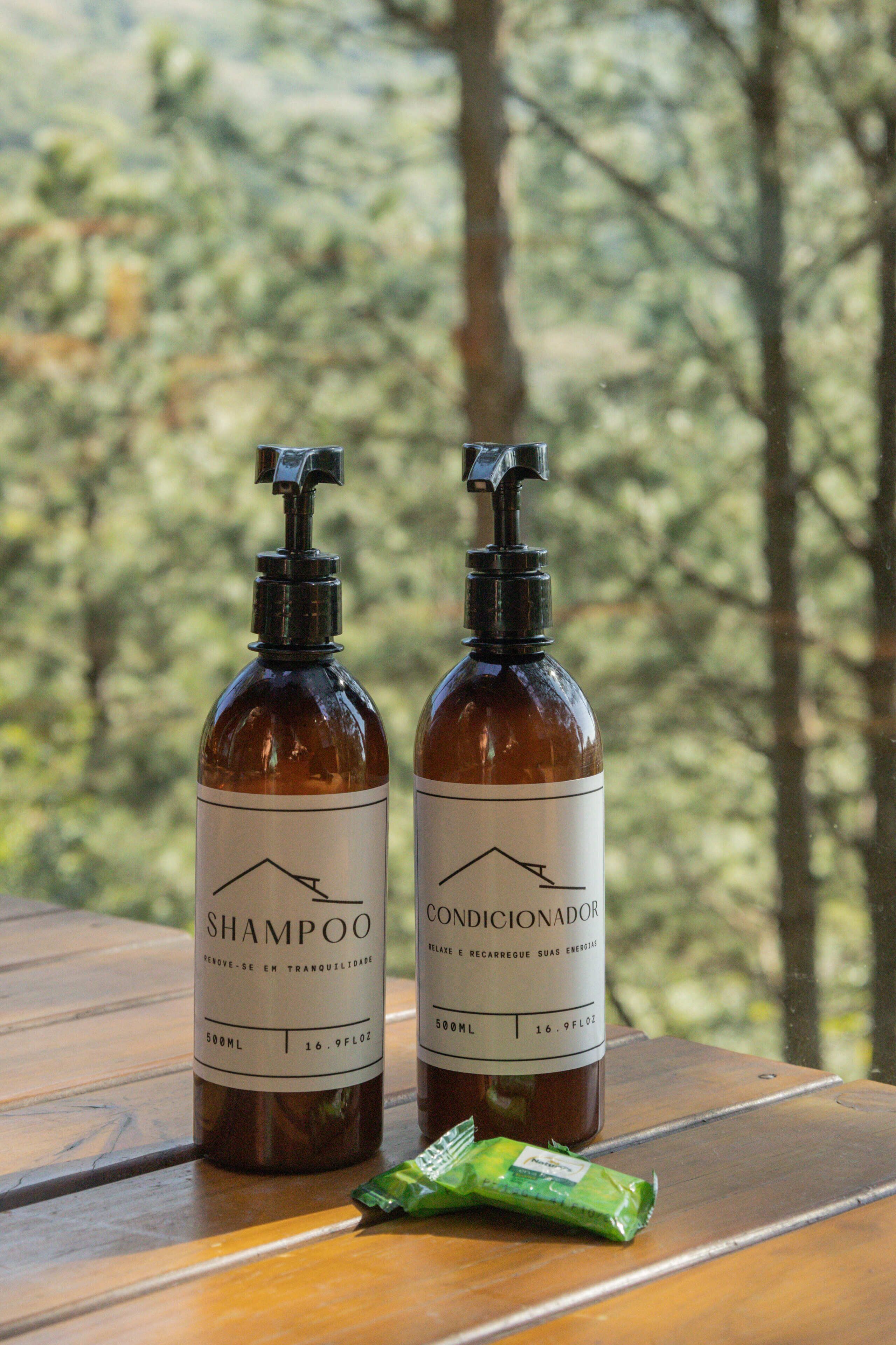 Duas garrafas de shampoo e condicionador sobre uma mesa de madeira, com vista para uma floresta.