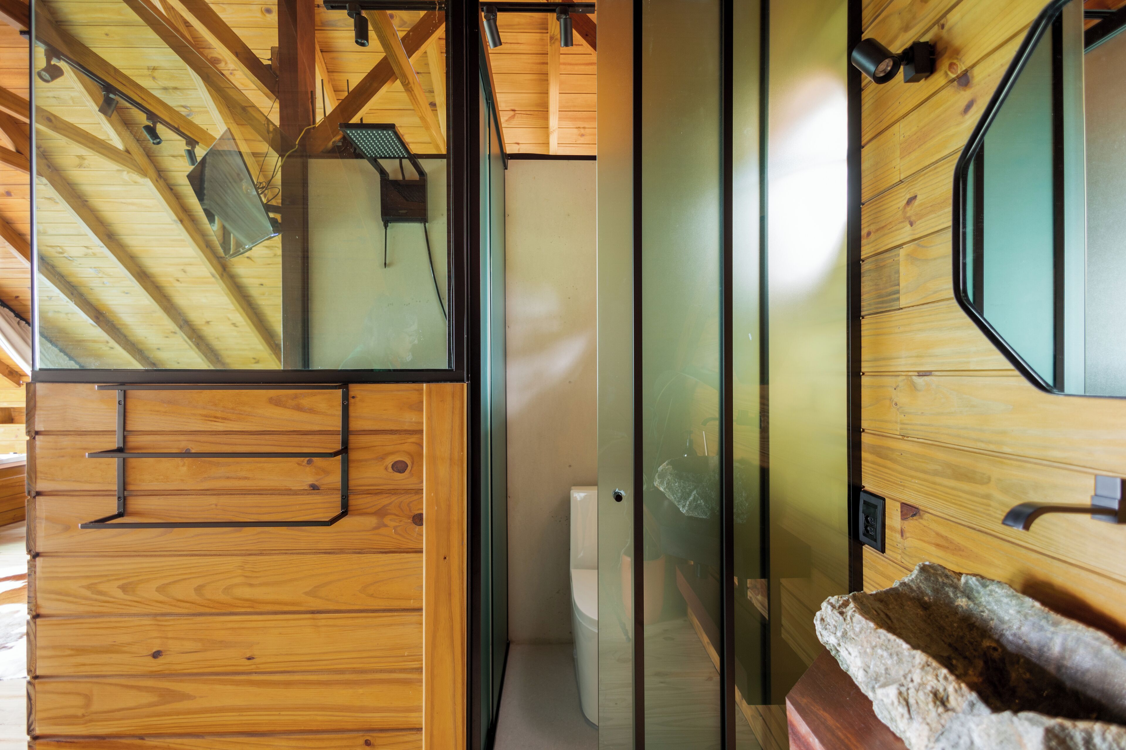 A wooden interior with a glass partition, a stone sink, and a wooden ceiling structure.
