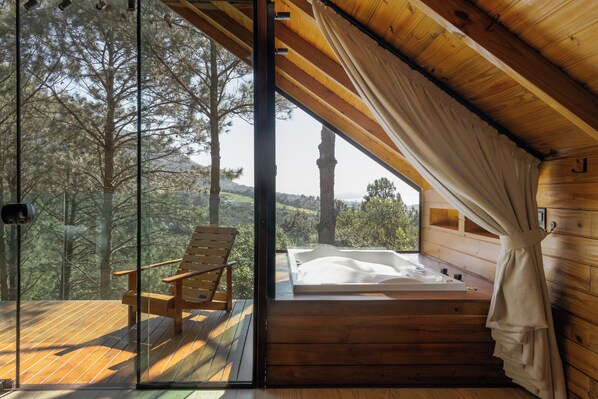 Une cabane en bois avec une porte en verre donnant sur un balcon, une chaise en bois et un jacuzzi.