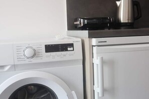 A compact kitchen with a washing machine, a coffee maker, and a microwave. - Athenean Porto Pireaus Suites-a1 (Pireas)