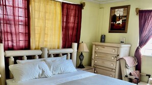 A bed with a wooden frame, a bedside table with a lamp, and a dresser with drawers. - COMFORTABLE KING BEDROOM FLAT in townhome in a pleasant Hilltop neighborhood, (Kingston 6)