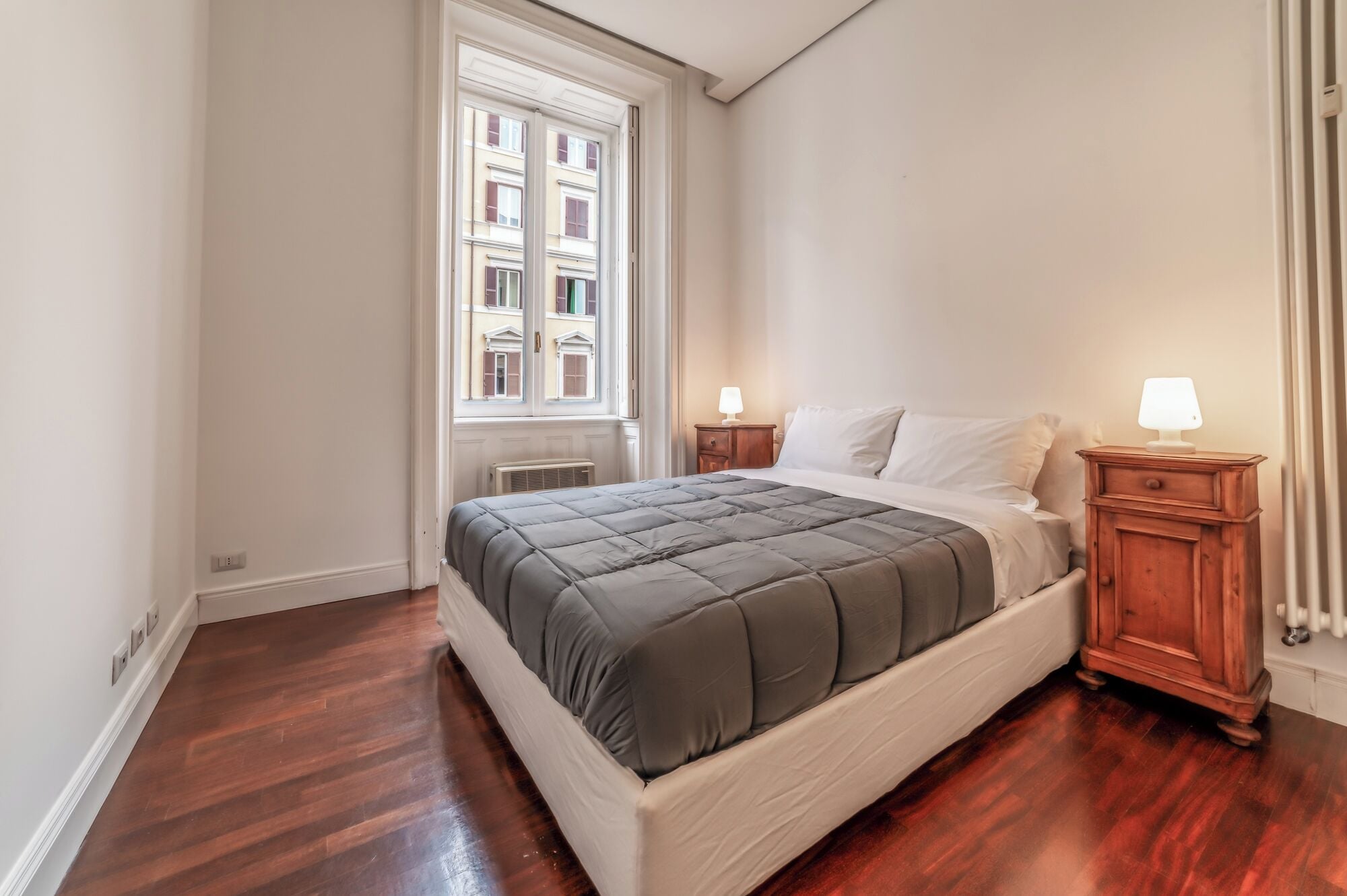 A bedroom with a bed, nightstands, a window, and a radiator.