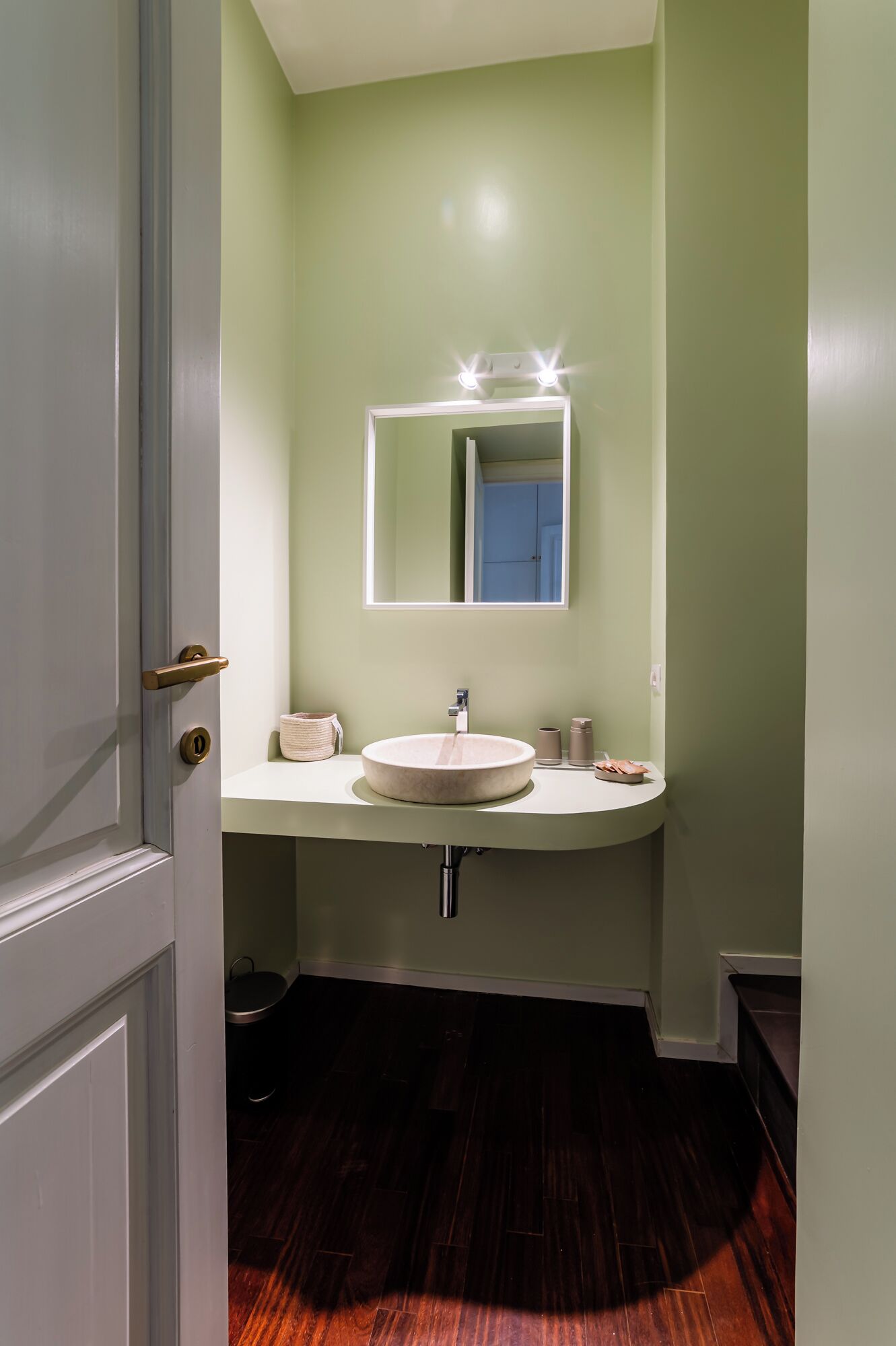 A bathroom with a white sink, a mirror with lights, and a wooden floor.