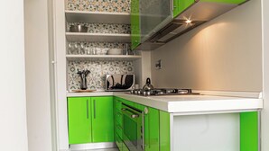 Une cuisine avec des meubles de couleur verte, un plan de travail blanc et un pare-feu en carreaux.
