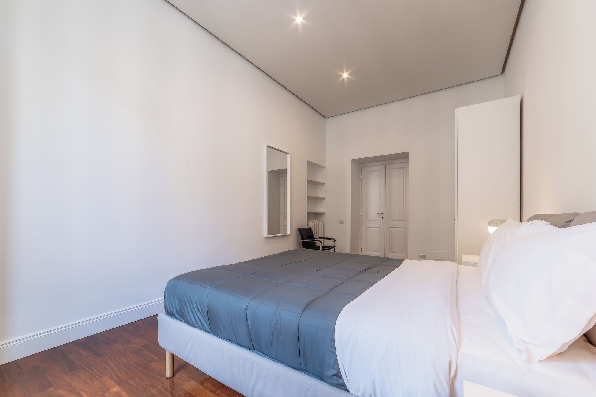 Een slaapkamer met een bed, een stoel, een deur en een spiegel.