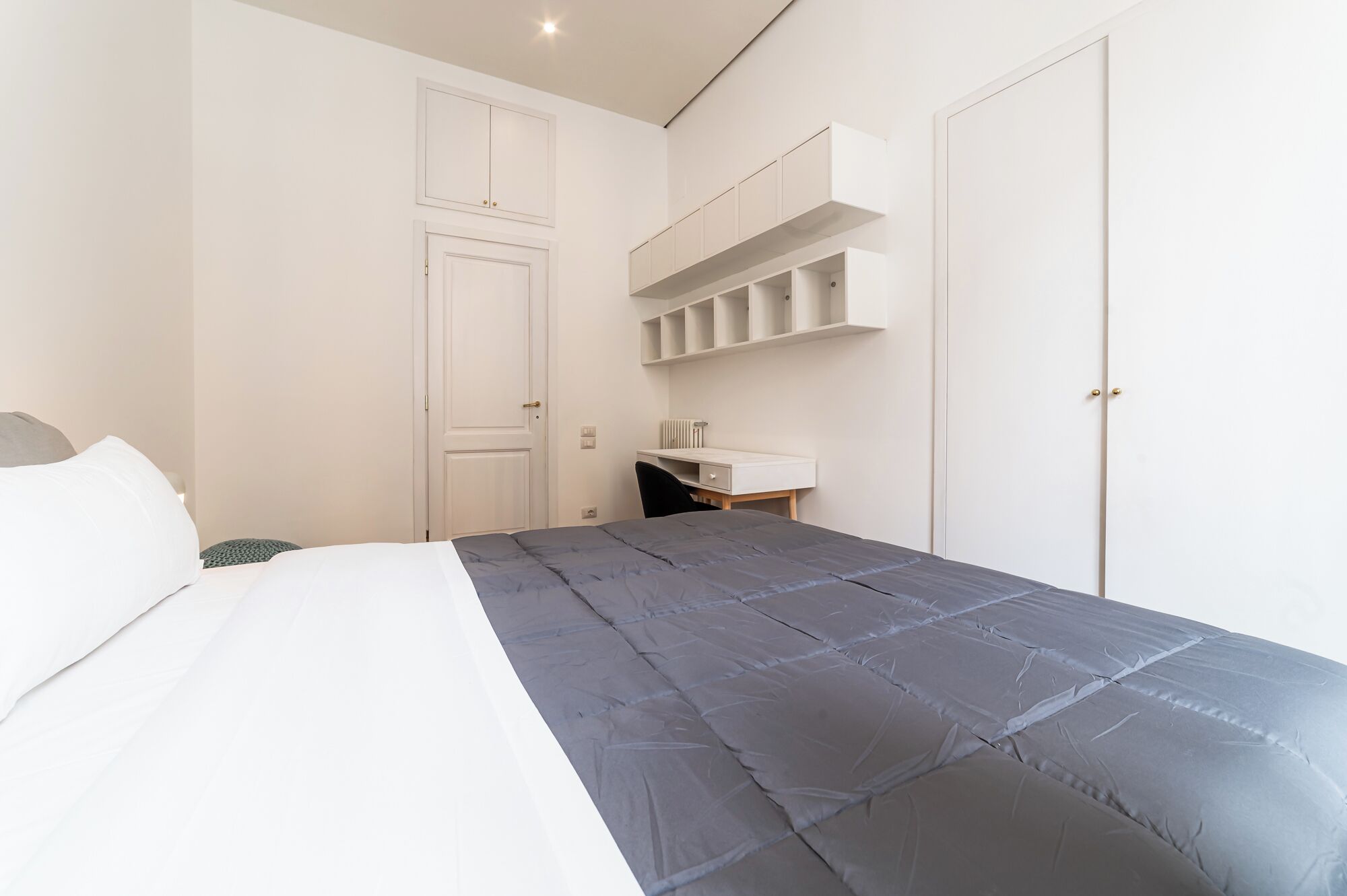 Ein Schlafzimmer mit Bett, Schreibtisch und eingebauten Regalen.