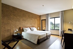 Een moderne hotelkamer met twee bedden, een bureau en een groot raam met uitzicht.