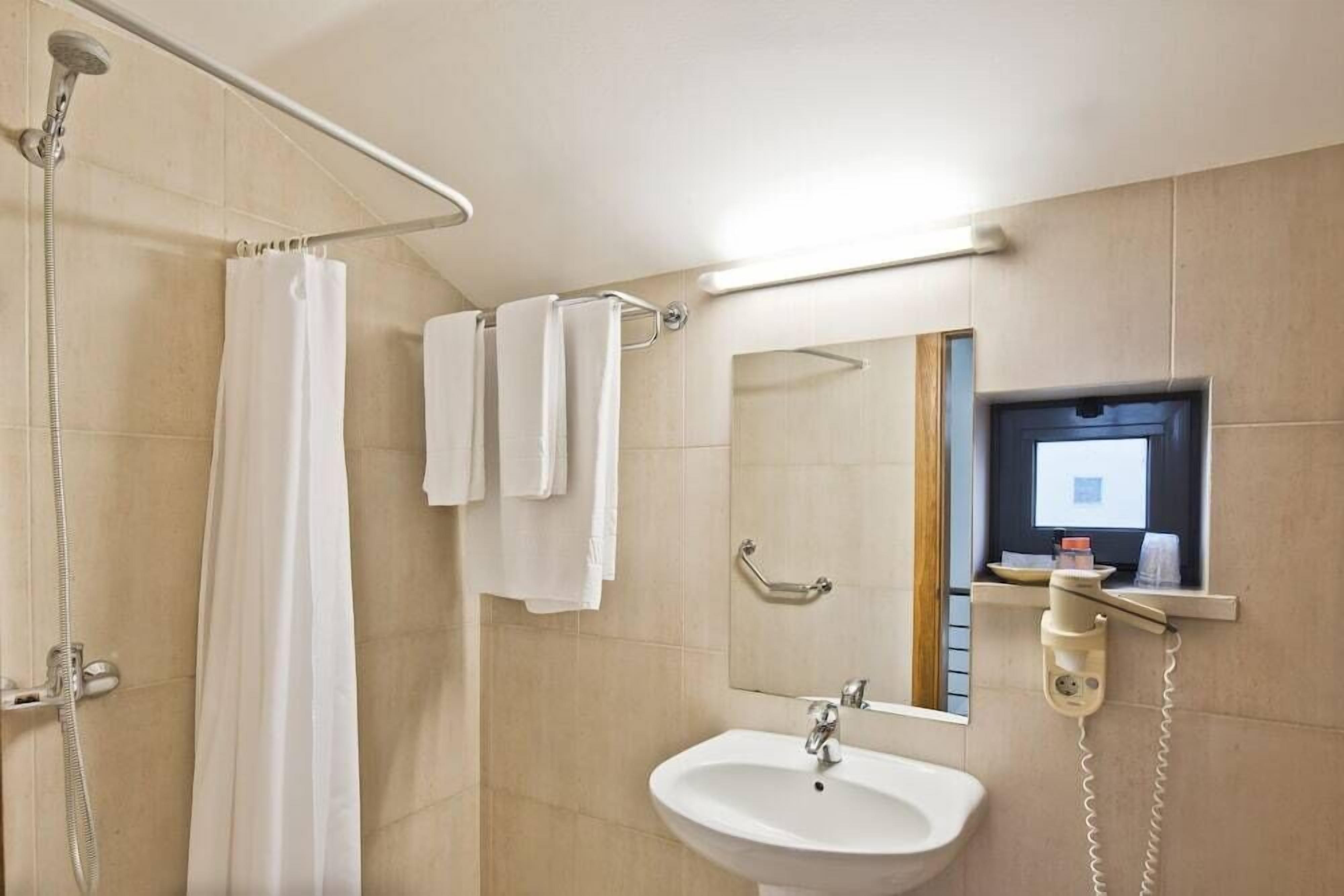 A bathroom with a shower, a sink, a mirror, and a wall-mounted phone.