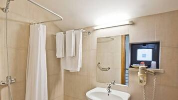 A bathroom with a shower, a sink, a mirror, and a wall-mounted phone.