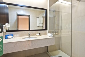Une salle de bain avec un grand miroir, un lavabo, une douche en verre et un porte-serviettes.