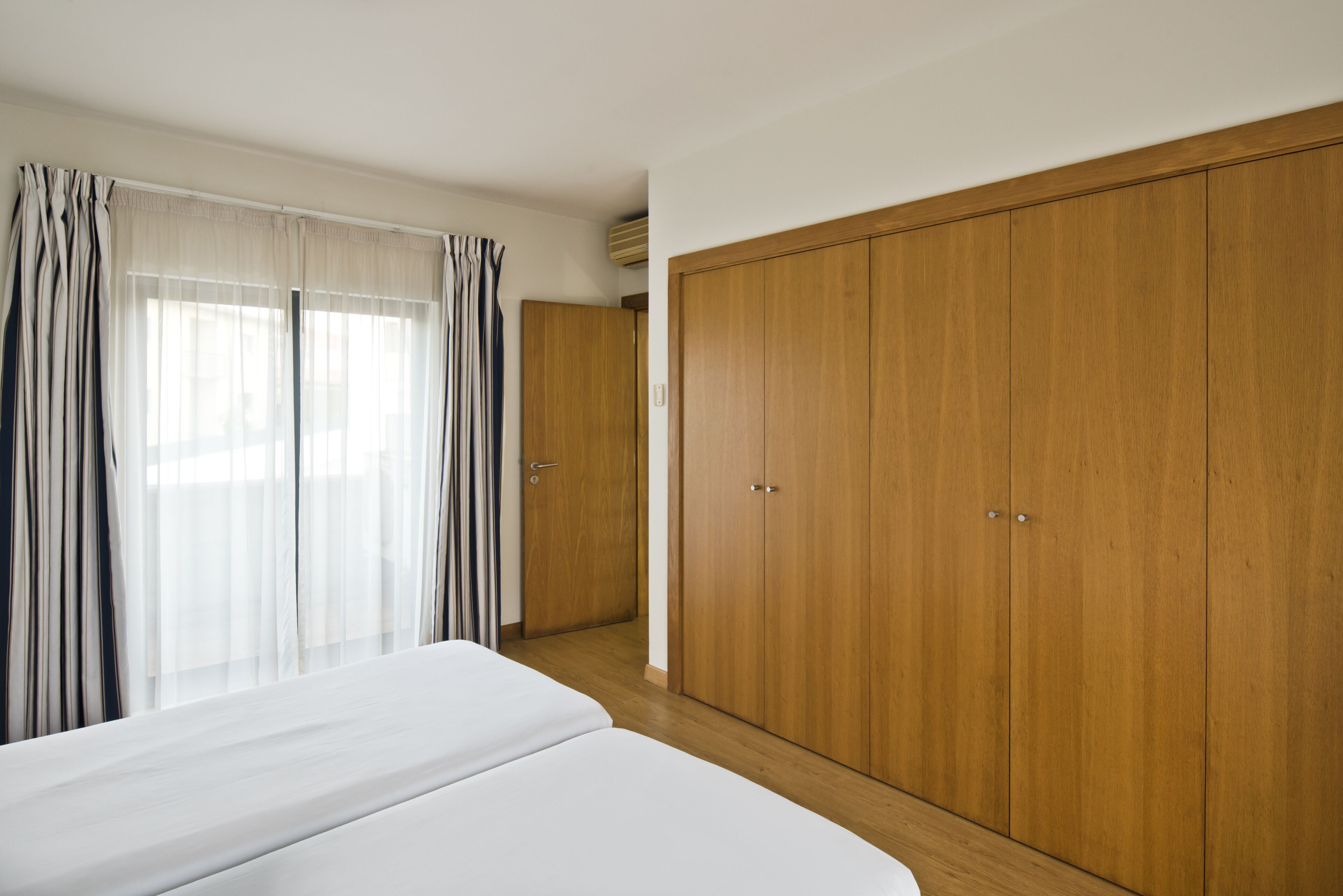 Une chambre à coucher avec un grand lit, une armoire en bois et une fenêtre avec des rideaux.