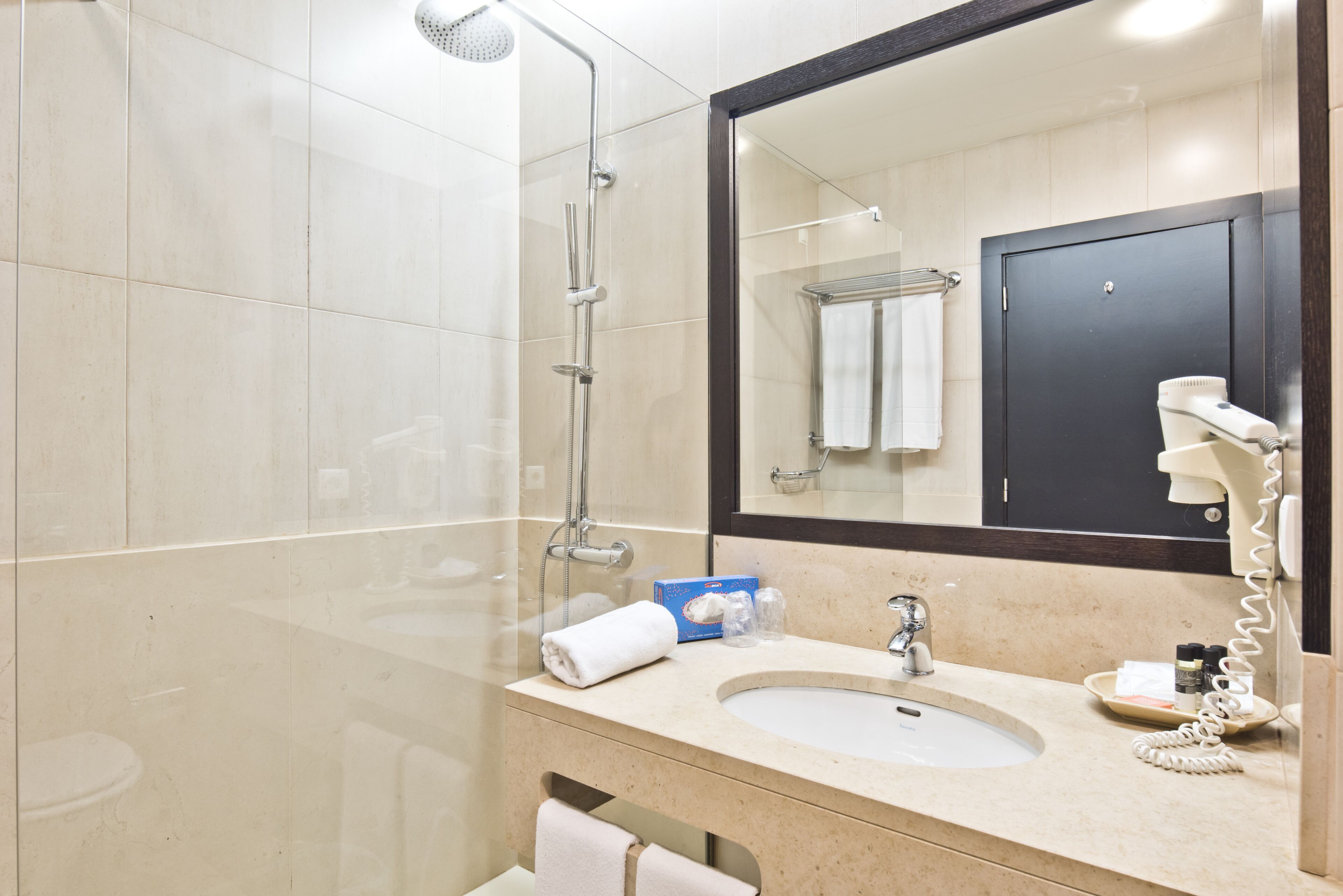 A modern bathroom with a glass shower enclosure, a sink with a mirror, and a hairdryer on the wall.