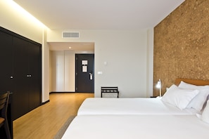 Een hotelkamer met een bed, nachtkastje, lamp en een deur naar een andere kamer.