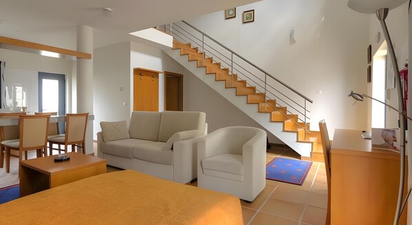 A modern living room with a sofa, armchairs, a coffee table, a staircase, and a dining area. - LAM Hotel Estarreja (Estarreja)