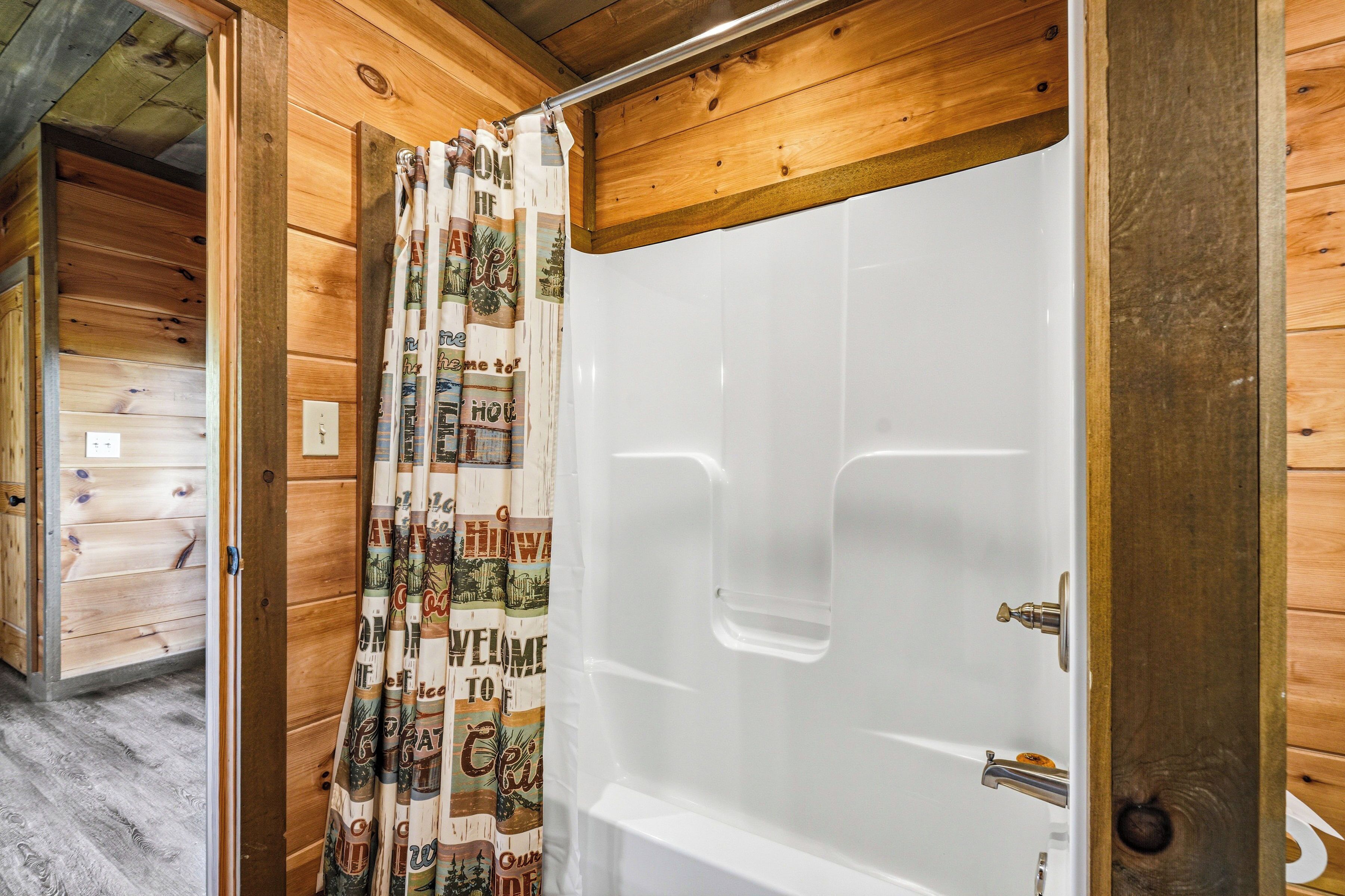 A wooden interior with a shower area featuring a white tub and a shower curtain with travel-themed prints.