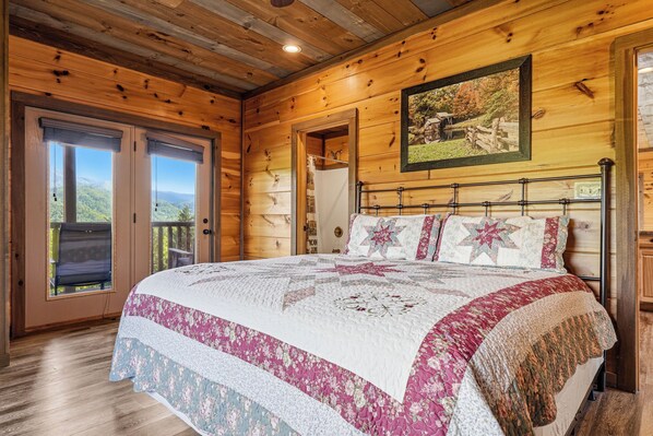 A wooden cabin bedroom with a large bed, a view through the door, and a painting on the wall. - New Listing, Stunning Views, Private Pool, Hot Tub, Games, Free Attractions! (Gatlinburg)