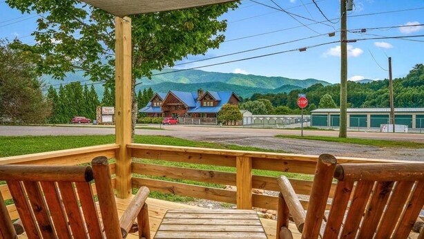 A wooden deck with two chairs, a stop sign, a building with a blue roof, and a mountain backdrop. - Whispering Pines | 3 Bedroom Suite | Pet Friendly! (Sevierville)