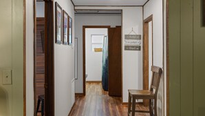 A hallway with wooden flooring, a chair, and a door leading to a room with a window and a basket on the sill. - Whispering Pines | 3 Bedroom Suite | Pet Friendly! (Sevierville)