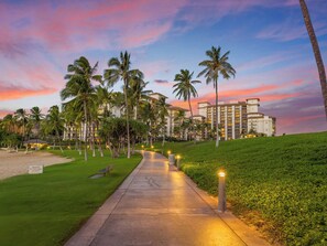 Ein Weg, der zu einem Hotel mit Blick auf den Strand führt, mit Palmen und einem Sonnenuntergangshimmel.
