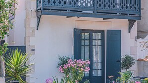En bygning med en mørkeblå dør, en balkon med et dekorativt gelænder og forskellige planter, herunder hortensiaer og en palme.