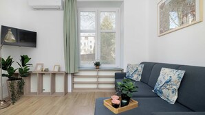 En moderne stue med sofa, fjernsyn, et vindue med udsigt og en plante på vindueskarmen.