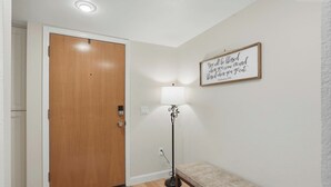 Un couloir avec une porte en bois, un banc, un lampadaire et un panneau fixé au mur.