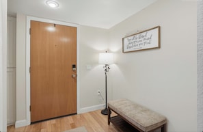 Ein Flur mit einer Holztür, einer Bank, einer Stehlampe und einem an der Wand befestigten Schild.