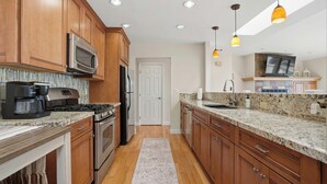 Une cuisine moderne avec des meubles en bois, des appareils électroménagers en acier inoxydable, des plans de travail en granit et des luminaires suspendus.