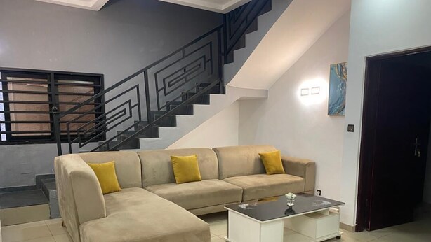 Una sala de estar con un sofá modular, una mesa de centro, una escalera y una puerta.