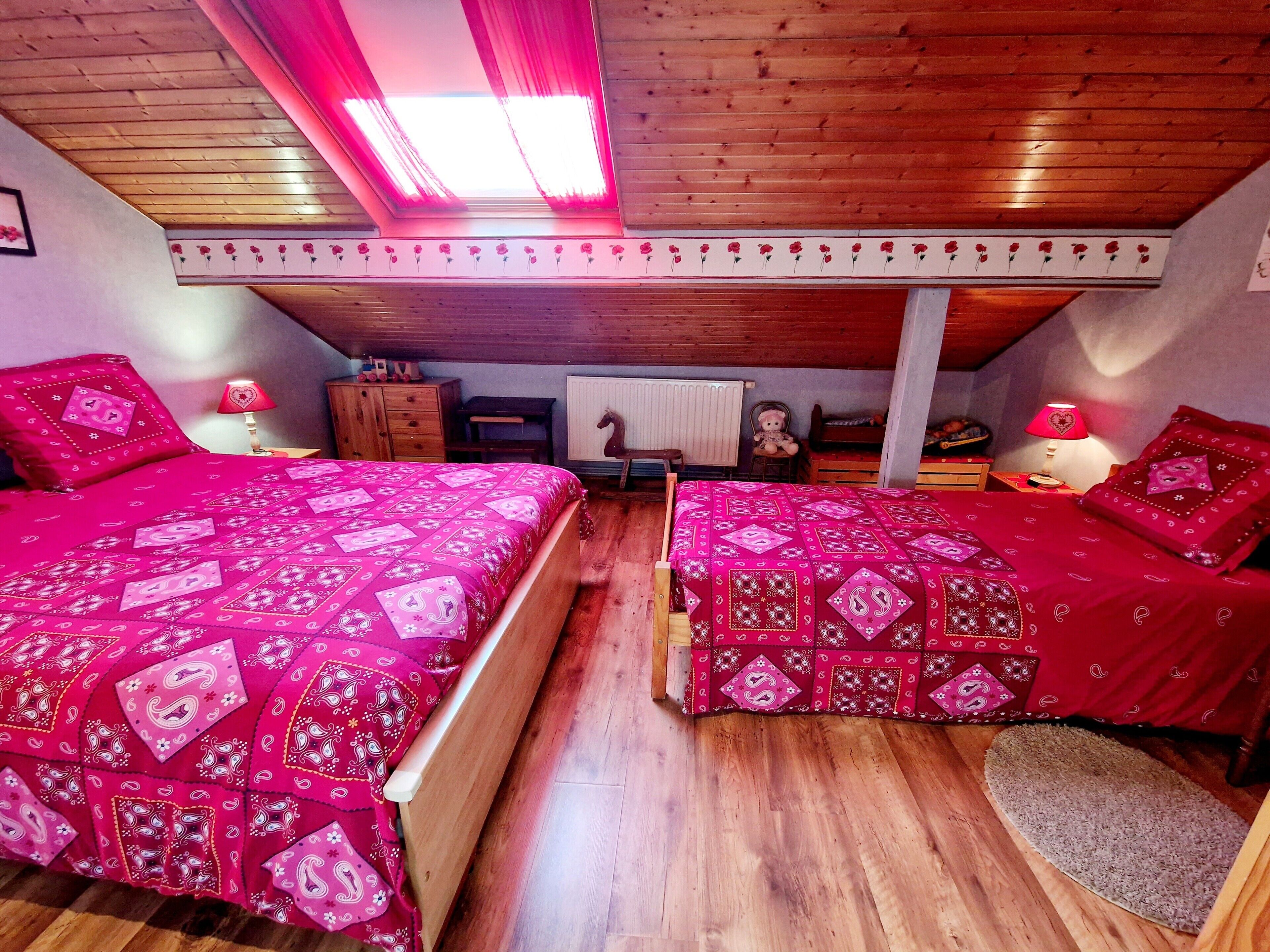 A bedroom with two beds, wooden flooring, a sloped ceiling with skylight, and a horse decoration.