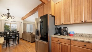 A kitchen with wooden cabinets, a stainless steel refrigerator, a coffee maker, and a dining area with a table and chairs.