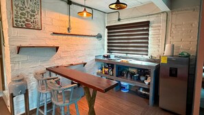 A kitchen with a wooden table, bar stools, hanging pendant lights, a refrigerator, and a window with blinds. - Modern and Cozy Rustic Loft (Puerto Vallarta)