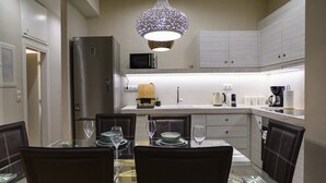 A modern kitchen with a dining table set for four, a refrigerator, microwave, and a hanging light fixture. - Boho 2 bdr luxury meets the East (Athina)