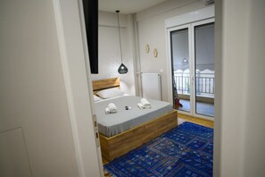 Une chambre avec un lit en bois, un tapis à motifs bleus, un luminaire suspendu et une vue sur un balcon doté d’une balustrade.
